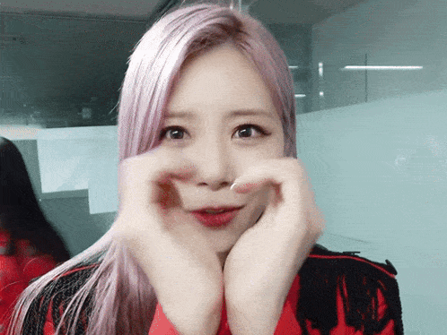 a woman with purple hair is making a heart shape with her hands