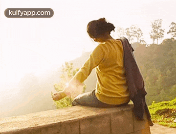 a woman is sitting on a wall with her arms outstretched and looking at the sun .
