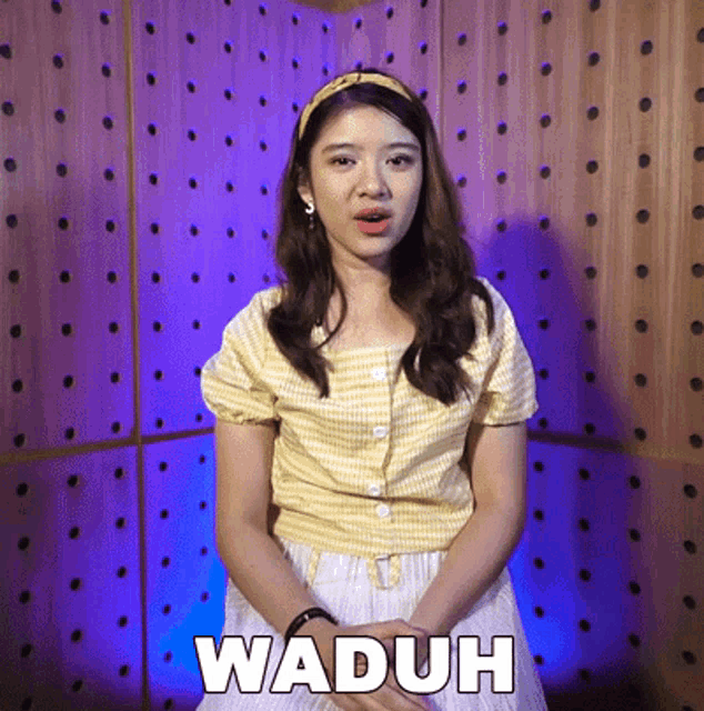a woman is standing in front of a wooden wall with the word waduh written on it
