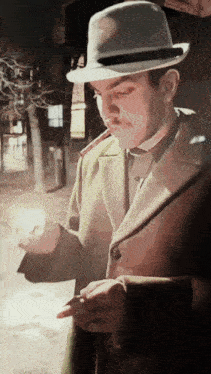 a man wearing a hat and a green coat is smoking a cigarette