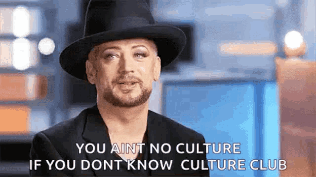 a man wearing a hat and a suit is saying `` you aint no culture if you dont know culture club '' .