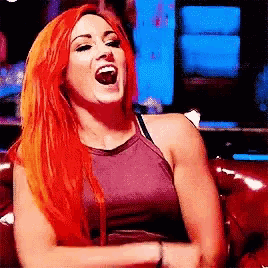 a woman with red hair is sitting on a red couch and laughing