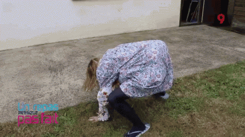 a woman in a floral dress is crawling in the grass in front of a building with the number 9 on it
