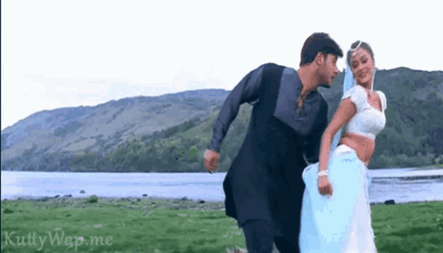 a man and a woman are dancing in a field with a lake in the background .