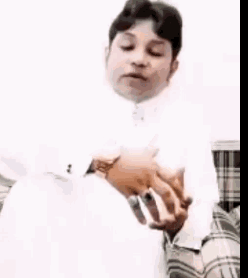 a man in a white shirt and tie is sitting on a couch holding something in his hands .
