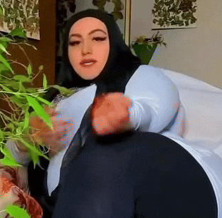 a woman wearing a hijab is sitting on a couch in front of a plant .