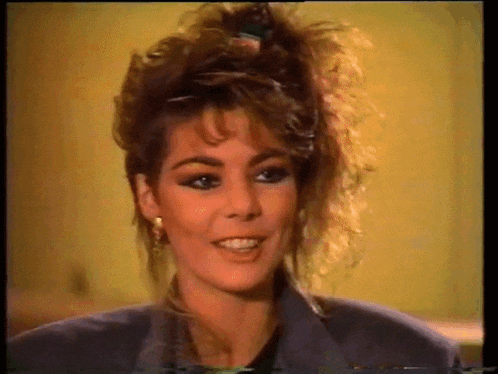 a woman with curly hair is smiling and wearing a grey jacket