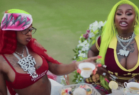 two women are sitting at a table with a cup of tea and one of them is wearing a red top that says big sexy
