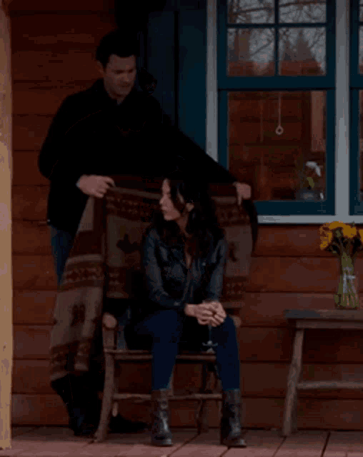 a man standing next to a woman sitting on a chair on a porch