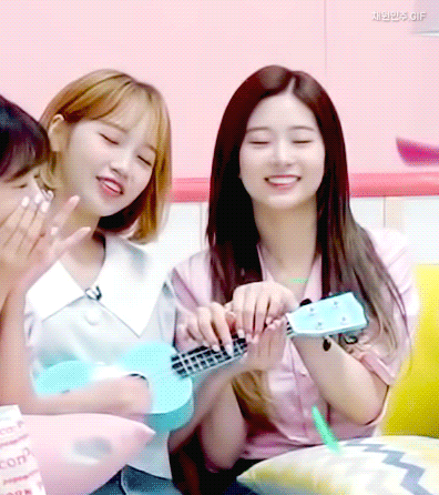 a girl is playing an ukulele while another girl looks on