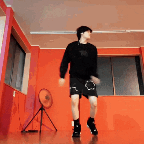 a man in a black shirt and black shorts is dancing in front of an orange wall