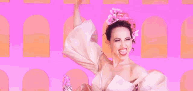 a woman in a white dress with a pink flower in her hair is dancing on a pink background .