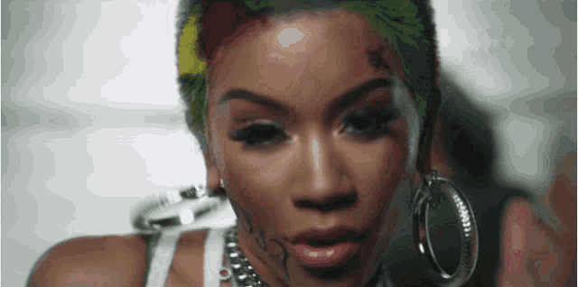 a woman with a tattoo on her face is wearing hoop earrings and a white tank top .