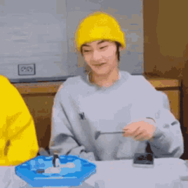 a man wearing a yellow beanie is sitting at a table playing a game with penguins .