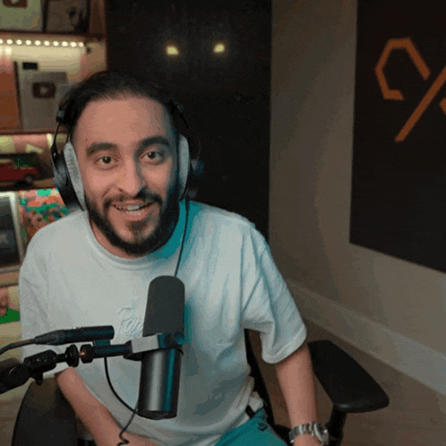 a man with a beard wearing headphones and a white t-shirt with a microphone behind him