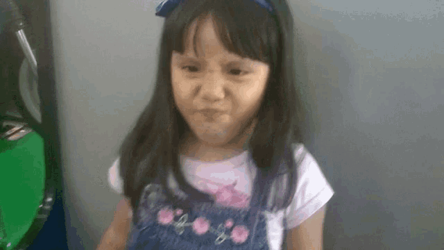a little girl wearing overalls and a headband is making a funny face