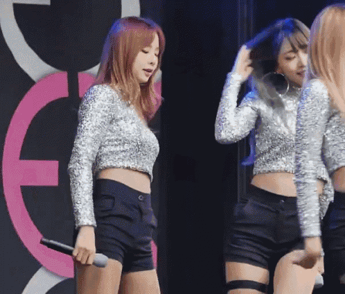 a woman in a silver top and black shorts is holding a microphone on stage