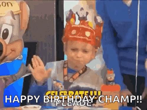 a young boy wearing a crown is sitting at a table with a chuck e cheese mascot .