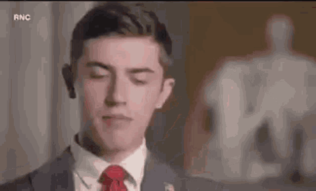 a man in a suit and tie is standing in front of a statue with his eyes closed .