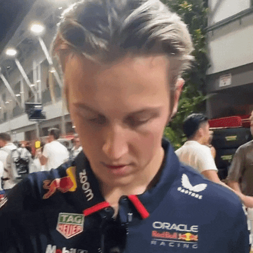 a man wearing a blue oracle red bull racing shirt looks down