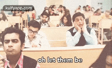 a group of people are sitting at desks in a classroom with their hands on their faces .