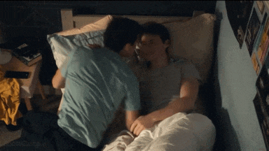 a couple of men are laying in bed and kissing each other .