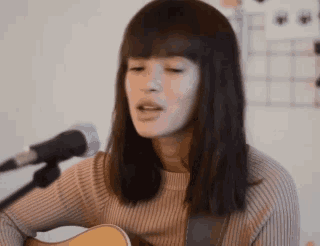 a woman is singing into a microphone while playing an acoustic guitar
