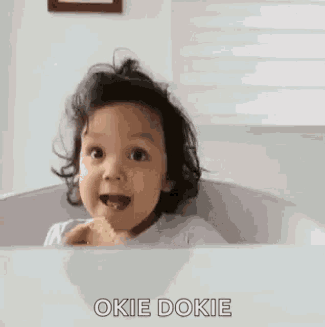 a baby is sitting in a bathtub eating a cookie and making a funny face .