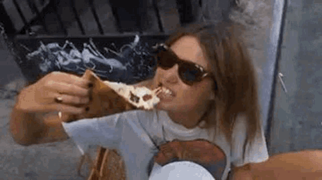 a woman wearing sunglasses is eating a large piece of pizza .