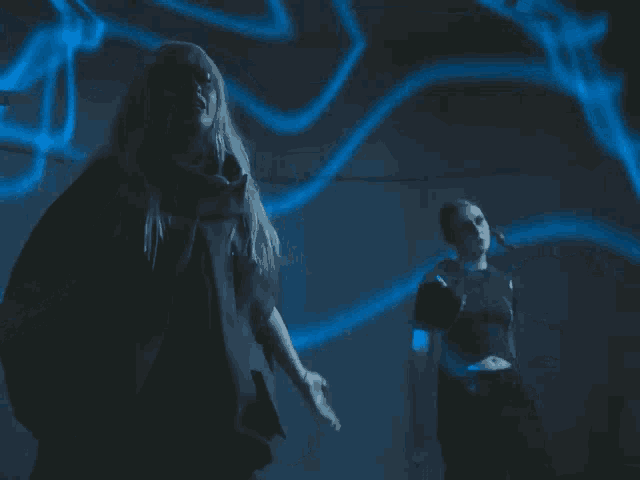 a woman with long blonde hair is standing in front of a blue light