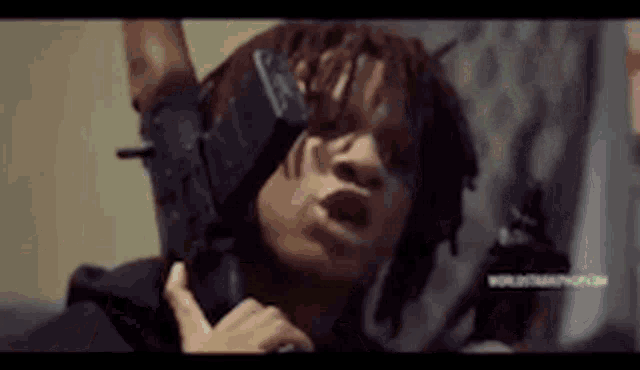 a man with dreadlocks is holding a gun in his hand and making a funny face .