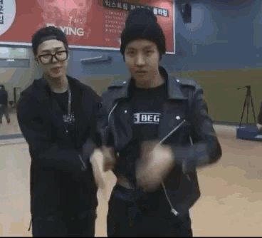 two young men are standing next to each other in a gym . one of the men is wearing a beanie and glasses .