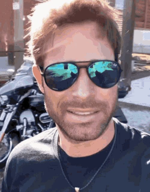 a man wearing sunglasses and a black shirt is smiling in front of a motorcycle