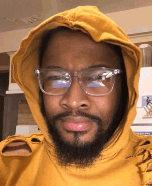 a man wearing glasses and a yellow hoodie looks at the camera