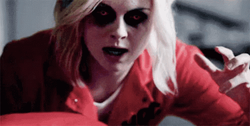 a woman in a red jacket with black eyes is looking at the camera with her hands outstretched .