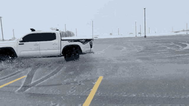 a white tacoma truck is driving through a parking lot in the snow