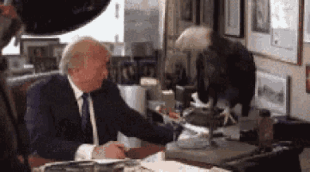 a man in a suit and tie is sitting at a desk in front of a statue of an eagle .