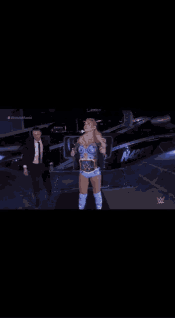 a woman with a wrestling belt is standing in front of a boat with the word nm on it .