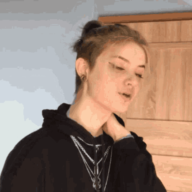 a girl wearing a black hoodie and a chain around her neck looks at the camera