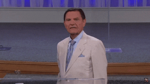 a man in a white suit and tie stands in front of a podium