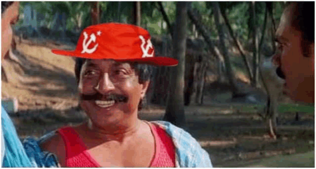 a man with a mustache is wearing a red hat with a communist symbol on it and smiling .