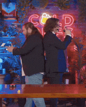 two men dancing in front of a neon sign that says cold