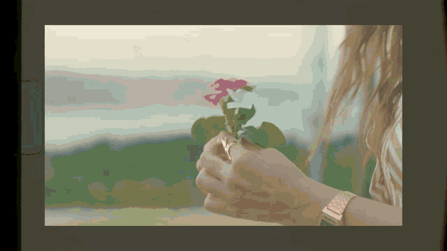 a woman wearing a watch is holding a pink flower in her hand