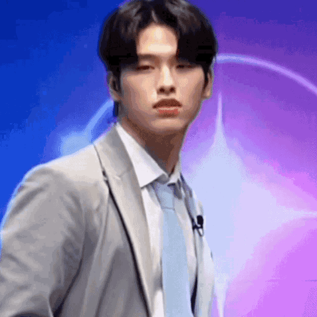 a man in a suit and tie is standing in front of a purple and blue background .