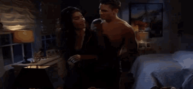 a shirtless man and a woman are hugging in a dark bedroom
