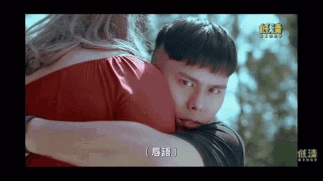 a man in a red shirt is hugging a woman with chinese writing on the screen behind them