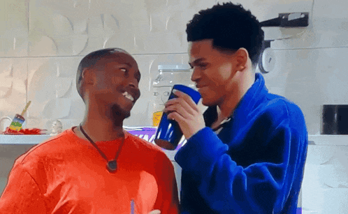a man in a blue robe is drinking from a blue cup next to another man
