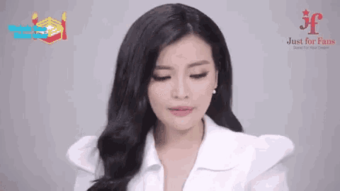 a woman with long black hair is wearing a white shirt and earrings and making a funny face .