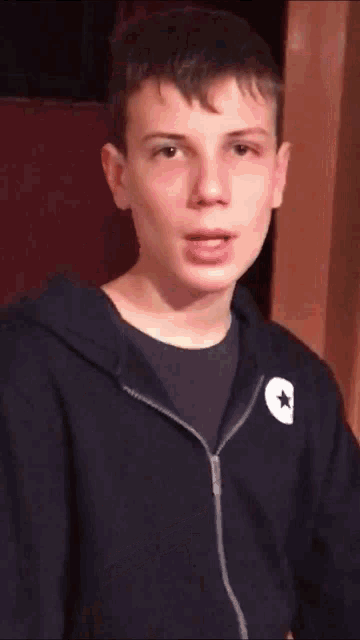 a young man wearing a black converse hoodie looks at the camera