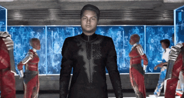 a man in a black suit is standing in front of a group of people in red jumpsuits